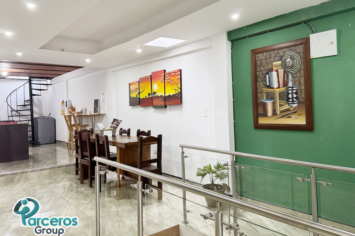Un comedor espacioso con techo alto, una escalera y una pared verde decorativa.
