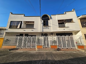 Un edificio de dos pisos con fachada blanca, una entrada protegida por una reja y un letrero que indica que es un hotel.