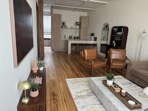 Ein modernes Wohnzimmer mit Holzboden, einer Couch, einem Couchtisch mit Dekoration und einer Küche im Hintergrund.