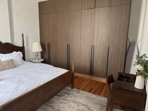 Une chambre à coucher comprenant un lit, une table de chevet, une lampe, une armoire, un bureau, une chaise et une plante en pot.