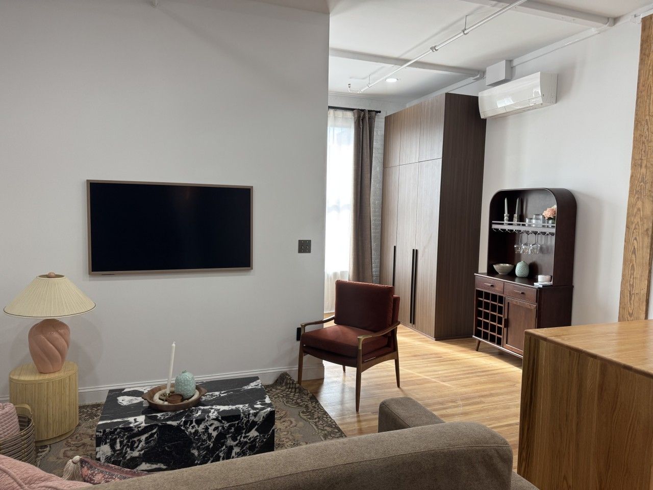 Un salon moderne avec un téléviseur à écran plat, un fauteuil rouge, un meuble en bois contenant de la verrerie et un tapis à motifs.