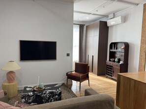 Ein modernes Wohnzimmer mit einem Flachbildfernseher, einem roten Sessel, einer Holzvitrine mit Gläsern und einem gemusterten Teppich.