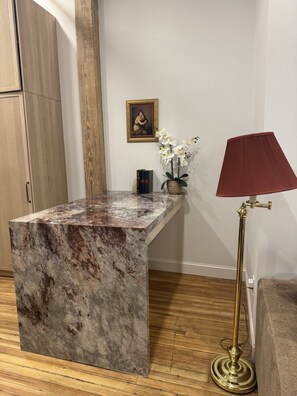 A marble reception desk, a framed painting, a potted orchid, and a floor lamp in a room with wooden flooring and white walls. - The Ilium Suite 308 - Luxury Studio in Downtown Troy (Troy)