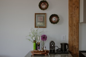 A kitchen with a wooden table, a coffee maker, a kettle, and two framed pictures on the wall. - Room 307, Ilium Luxury 2 Bd. (Troy)