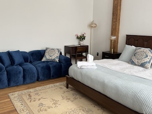 Ein Schlafzimmer mit einem Bett, einem blauen Sofa, einem kleinen Tisch mit einer Vase und einer Stehlampe.