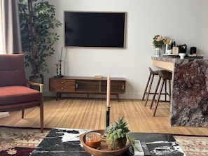A modern living room with a red chair, a wooden bench, a marble accent wall, and a large flat-screen TV mounted on the wall. - The Ilium Suite 304 - River view Luxury 1 bd Suite in Downtown Troy (Troy)