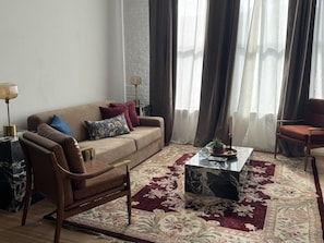 Ein Wohnzimmer mit Sofa, Sesseln, Couchtisch und einem gemusterten Teppich.