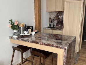 A kitchen with a marble countertop, wooden stools, and a backsplash with a marble pattern. - The Ilium Suite 304 - River view Luxury 1 bd Suite in Downtown Troy (Troy)