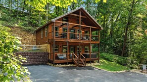 Een houten chalet met twee verdiepingen en een balkon, omgeven door bomen.