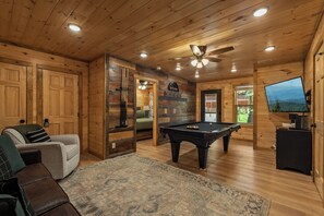 Een houten interieur met een pooltafel, een bank en een televisie.