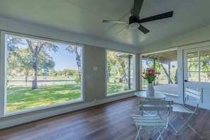 Una habitación con ventanas amplias, un ventilador de techo y una mesa con sillas.