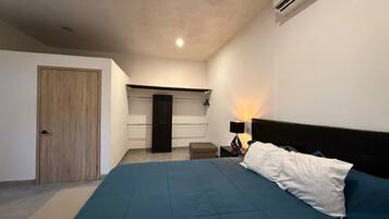 A bedroom with a bed, a nightstand, a lamp, a wardrobe, and a door.