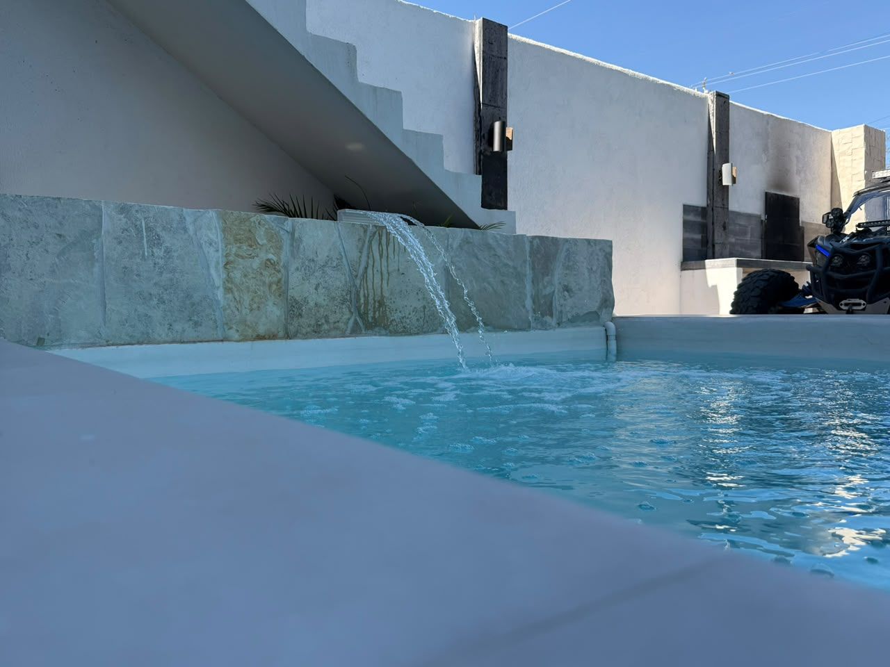 A swimming pool with a waterfall feature, a modern architectural design, and a vehicle parked nearby.