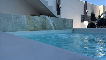 A swimming pool with a waterfall feature, a modern architectural design, and a vehicle parked nearby.