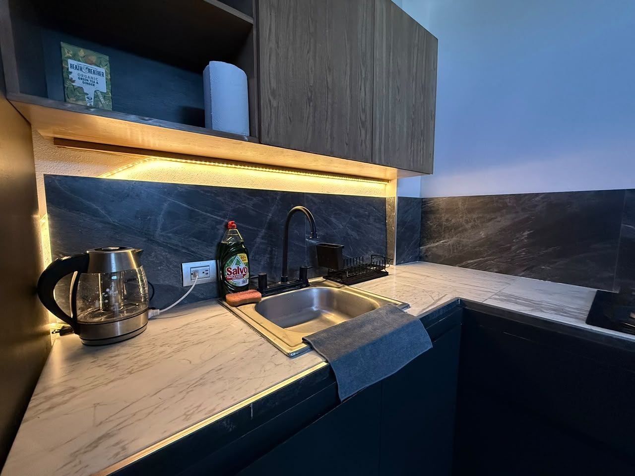 Een moderne keuken met een marmeren aanrecht, een roestvrijstalen waterkoker, een fles afwasmiddel en een spoelbak.