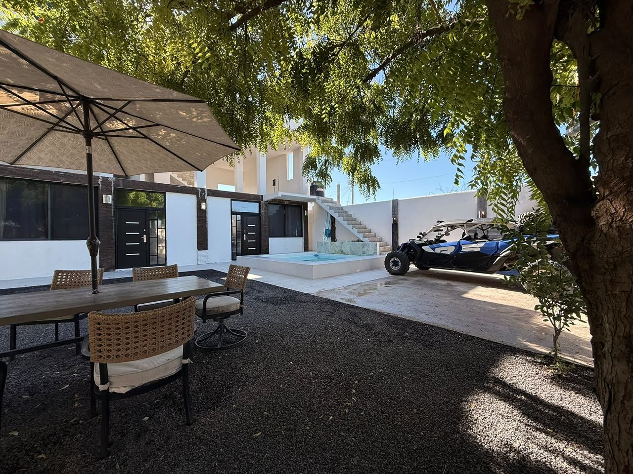 An outdoor seating area with a table and chairs, a covered umbrella, and a vehicle parked nearby.