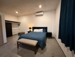 Une chambre à coucher comprenant un lit, des tables de chevet, un banc, un appareil de climatisation et une armoire.