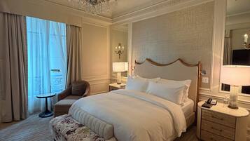 A hotel room with a large bed, a sitting area with a chair, a small table, and a nightstand with a lamp.