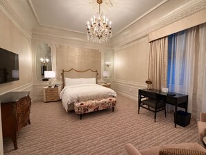 Een hotelkamer met een groot bed, een bureau, een kast en een kroonluchter.