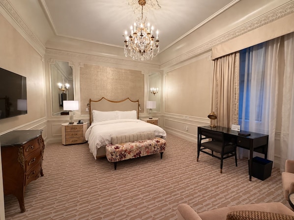 Ein Hotelzimmer mit einem großen Bett, einem Schreibtisch, einem Schminktisch und einer Kandelaber.