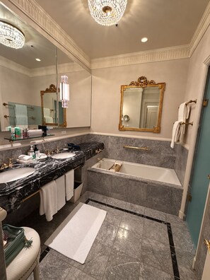 Een luxe badkamer met marmeren aanrechtbladen, een badkuip en een grote spiegel.
