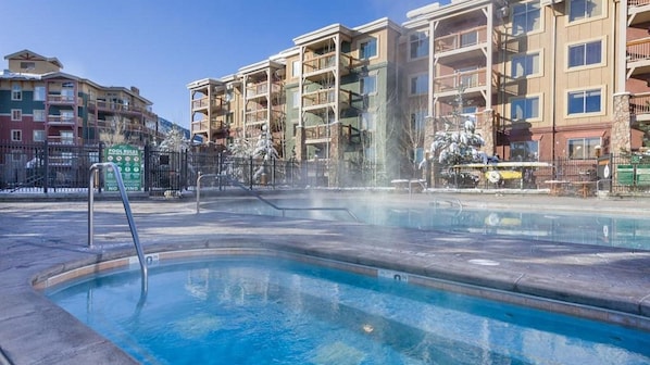 Piscina com hidromassagem, cercada por edifícios altos com varandas.