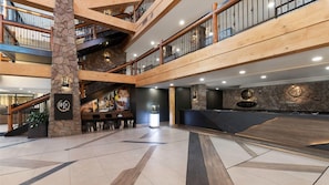 Um hall de vários níveis com parede de pedra, guarda-corpos de madeira e um balcão de recepção.