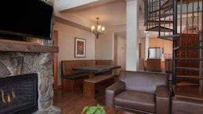 A living room with a stone fireplace, a television, a bench, a sofa, and a staircase. - Westgate Park City 4BR Villa - Private Hot Tub Balcony, Ski-In/Ski-Out (Park City)