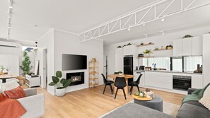 A modern living room with a fireplace, a dining area, and a kitchen with white cabinetry and black appliances. - 10 Hobson - Coastal Retreat (Queenscliff)