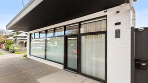 A modern building with large glass windows, a white brick exterior, and a black metal gate. - 10 Hobson - Coastal Retreat (Queenscliff)