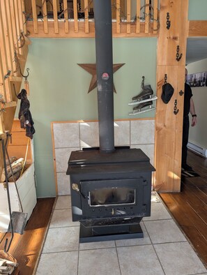 A wood-burning stove with a star decoration above it, a wooden shelf with boots, and a wall-mounted hat rack.