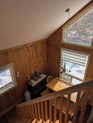 A wooden interior with a dining table, chairs, and a window with a view of snow-covered trees.