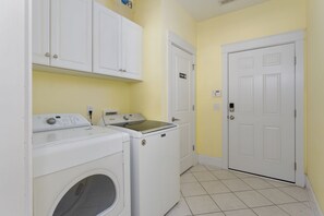 A laundry room with two washing machines and a dryer, a private door, and a thermostat on the wall. - Hot Dogs in Paradise - Carolina Beach Getaway (Carolina Beach)