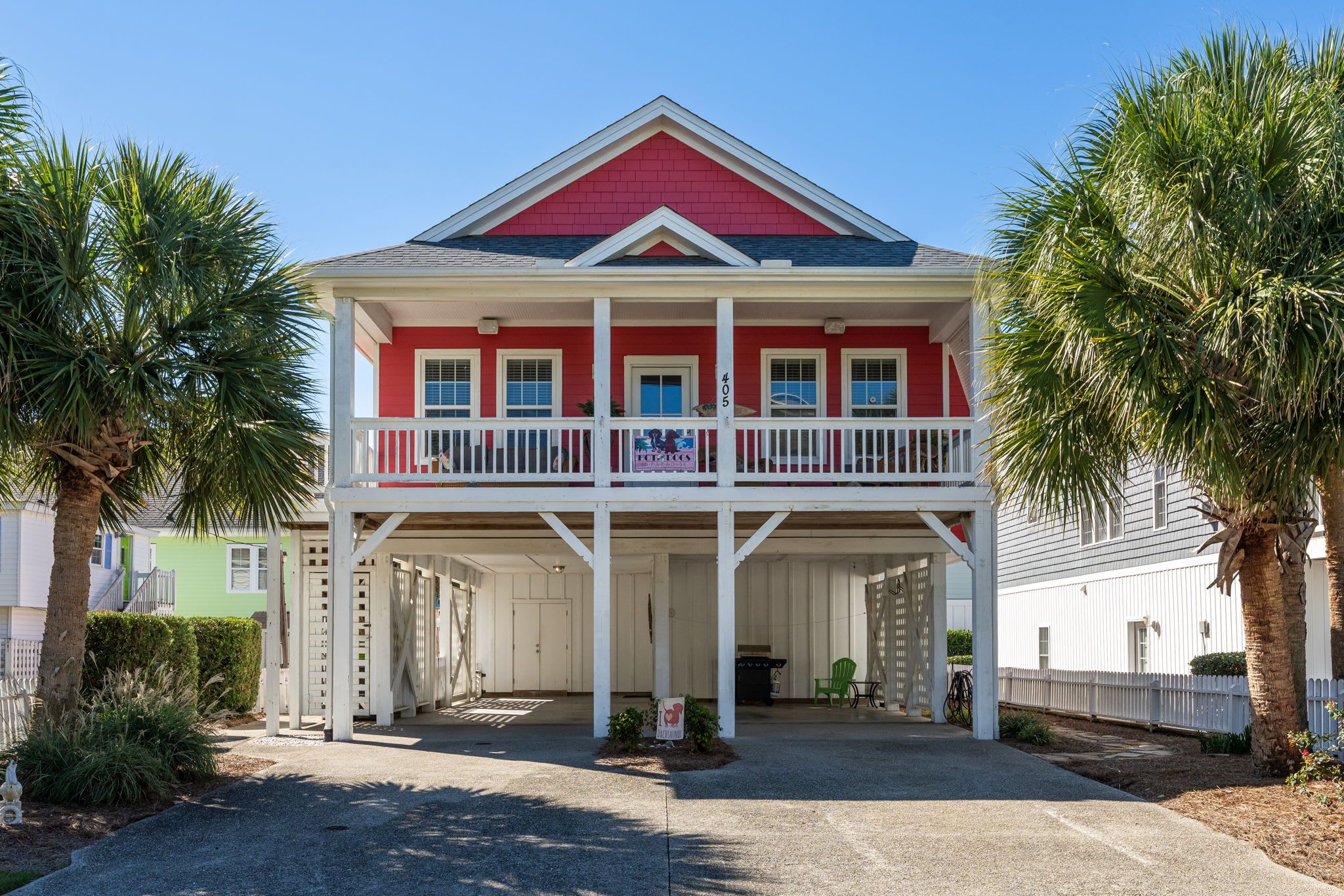 A two-story house with a red facade, white balcony railings, and a covered porch area.