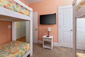 A bedroom with bunk beds, a television, a bedside table with a lamp, and a door leading to another room. - Hot Dogs in Paradise - Carolina Beach Getaway (Carolina Beach)