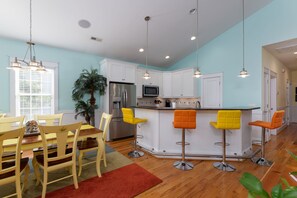 A modern kitchen with white cabinets, stainless steel appliances, and a central island with bar stools. - Hot Dogs in Paradise - Carolina Beach Getaway (Carolina Beach)