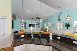 A kitchen with a granite countertop, a sink, and a dining area with chairs. - Hot Dogs in Paradise - Carolina Beach Getaway (Carolina Beach)