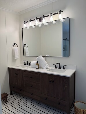 A bathroom with a large mirror, two sinks, wooden vanity, and a patterned floor.