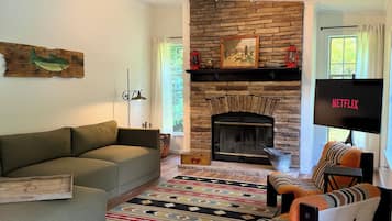 A living room with a stone fireplace, a sofa, a patterned rug, and a television.