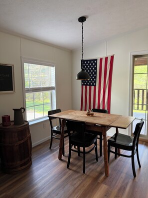 A dining area with a wooden table and chairs, an American flag, and a hanging light fixture.