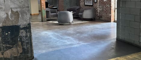 A spacious interior with a concrete floor, wooden accents, and a brick wall. There are seating areas with modern chairs and a neon sign.
