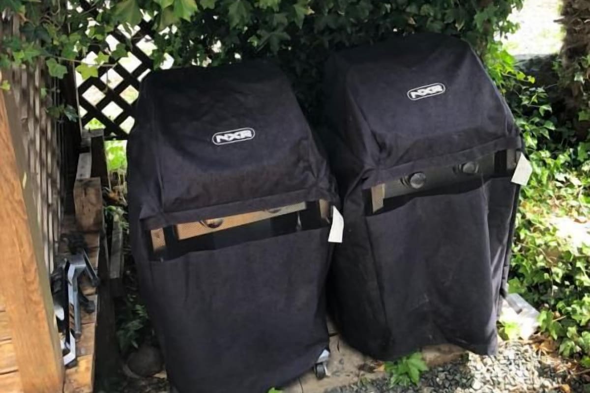 Deux barbecues noirs installés à l’extérieur, sous une pergola en bois recouverte de lierre.