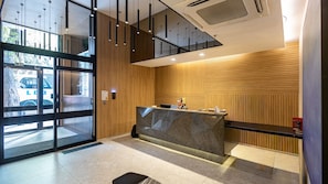 A reception area with a wooden panel wall, a reception desk, and a glass door entrance. - Skylux Downtown Rio With Rooftop Pool, Coworking Space, Gym, and Easy Access to the Subway by Carpediem (Rio de Janeiro)