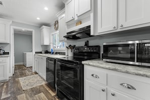 A modern kitchen with white cabinetry, a black stove, a microwave, and a dishwasher. - Fin & Feather - Steinhatchee Florida (Steinhatchee)