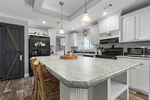 A modern kitchen with white cabinetry, a large island, and stainless steel appliances. - Fin & Feather - Steinhatchee Florida (Steinhatchee)