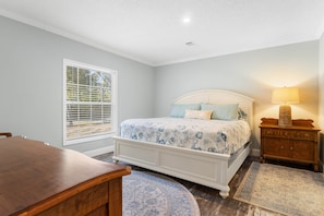 A bedroom with a bed, bedside table, lamp, window, and a wooden desk. - Fin & Feather - Steinhatchee Florida (Steinhatchee)