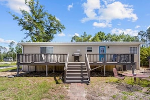 A single-story mobile home with a front porch, a set of stairs leading to the entrance, and a small patio area with outdoor seating. - Hatchee Haven - Home in Steinhatchee (Steinhatchee)