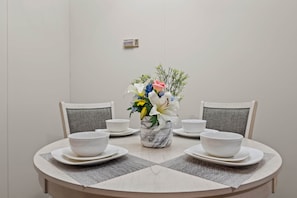 A dining table with white bowls and plates, a marble vase with flowers, and grey upholstered chairs. - Keaton Hideaway - Home in Keaton (Taylor County)