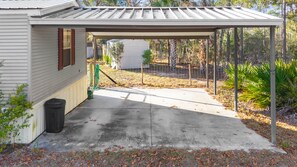 A covered garage with a concrete driveway, a wooden door, and a trash can. - Kings Creek Fish Camp - Steinhatchee Florida (Steinhatchee)