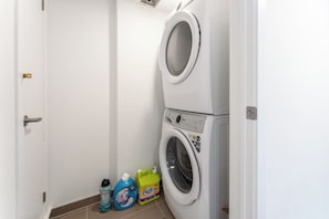 A laundry room with a front-loading washer and dryer, a door, and two bottles of laundry detergent.